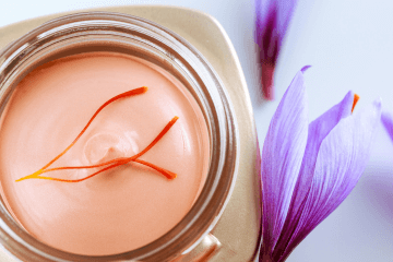 Vue sur un pot de crème hydratante avec trois stigmate posé dessus et des fleurs de safran posées à côté.